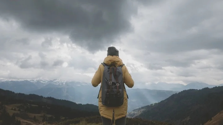 Young Caucasian female hiker in yellow raincoat wearing backpack enjoys the mountain view in French Alps